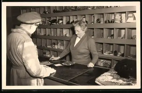 Fotografie Schuhmacher-Reparaturgeschäft, Dame hinter Verkaufstresen wickelt Geschäft mit Soldat ab