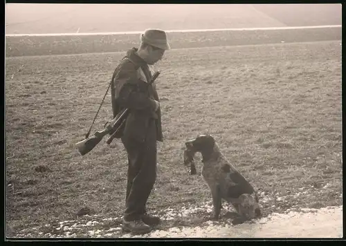 Fotografie Jäger mit Gewehr lobt Jagdhund nach dem aportieren eines Vogel's
