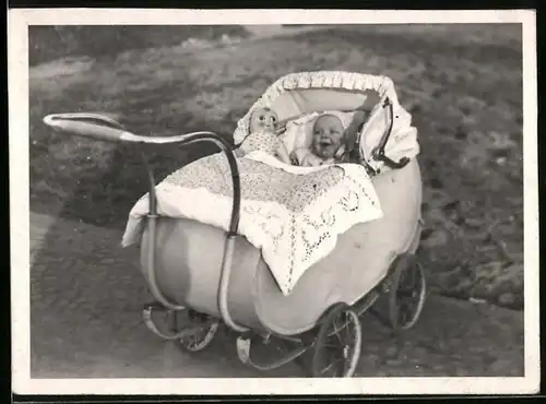Fotografie lachendes Baby mit Puppe im Kinderwagen liegend