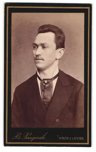 Fotografie B. Pasquali, Arco, Junger Mann mit Schnurrbart und schwarzer Krawatte mit Anstecker
