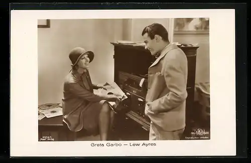 AK Schauspielerin Greta Garbo mit Hut im Kostüm auf Tisch sitzend u. Schauspieler Lew Ayres