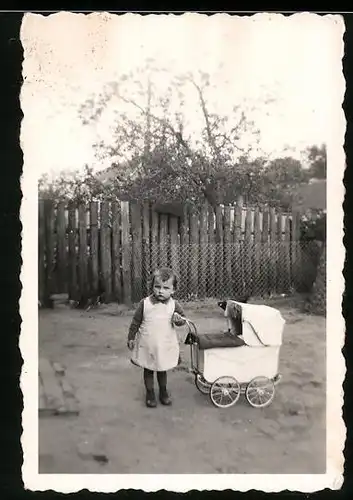 Fotografie Mädchen spielt mit Puppenwagen im Garten