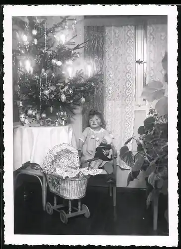 Fotografie Weihanchten, Mädchen mit Puppe und Puppenwagen unterm Weihnachtsbaum sitzend