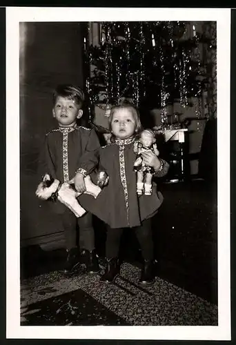 Fotografie Weihnachten, Knabe mit Stoffhund & Mädchen mit Puppe vor Weihnachtsbaum stehend