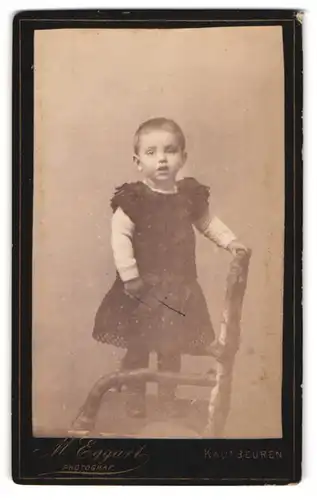 Fotografie M. Eggart, Kaufbeuren, Schrader Strasse, Kleines Kind mit kurzen Haaren im Kleid auf einem Stuhl