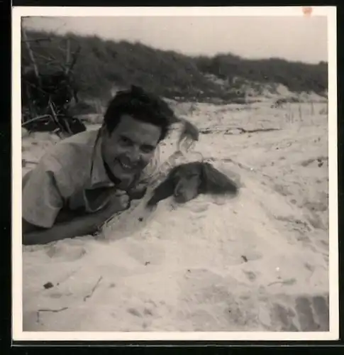 Fotografie Bursche hat Hund Dackel am Strand bis auf den Kopf eingebuddelt