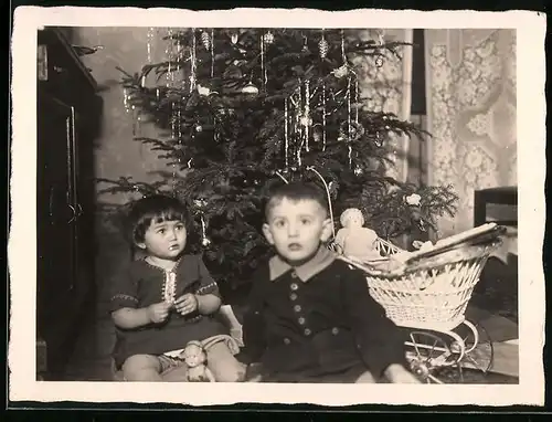 Fotografie Weihnachten, Knabe & Mädchen mit Puppe & Puppenwagen am Weihnachtsbaum sitzend