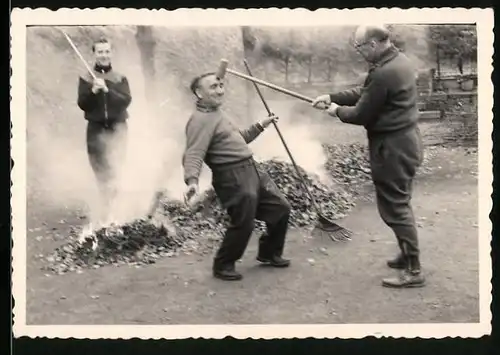Fotografie Männer verbrennen Gartenabfälle und albern mit Crocket-Schläger herum