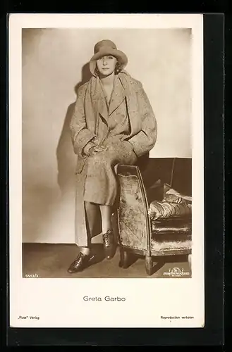 AK Schauspielerin Greta Garbo im Mantel mit Hut auf einer Sessellehne sitzend
