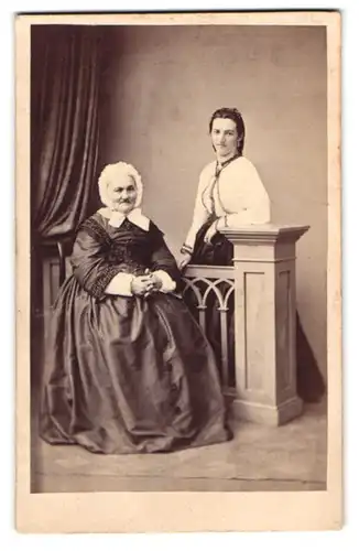 Fotografie unbekannter Fotograf und Ort, Portrait Grossmutter mit haube im Biedermeierkleid nebst Enkeltochter