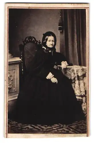 Fotografie J. Giese, Itzehoe, betagte Grossmutter mit Haube trägt weites schwarzes Kleid