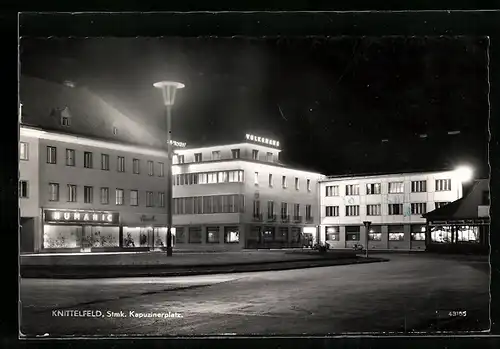 AK Knittelfeld /Stmk., Kapuzinerplatz mit Volkshaus und Geschäften bei Nacht