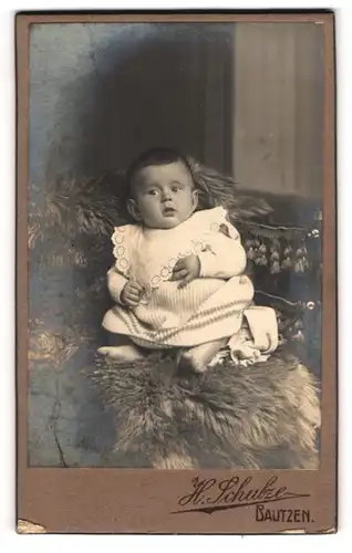 Fotografie H. Schulze, Bautzen, Kleines Kind im Kleid sitzt auf Fell