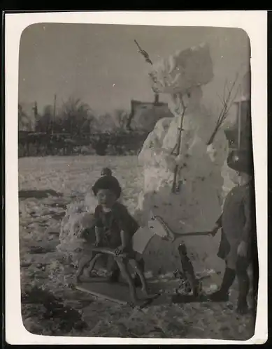 Fotografie Knaben spielen mit Holzpferd neben Schneemann im Winter