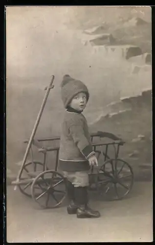 Fotografie überraschter Knabe mit Bollerwagen vor Studiokulisse