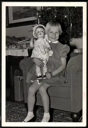 Fotografie Weihnachten, lachendes Mädchen mit Puppe unterm Weihnachtsbaum sitzend