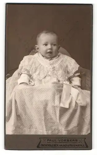 Fotografie Paul Vorberg, Oschersleben, Baby in weissem Spitzenkleid auf Sessel sitzend
