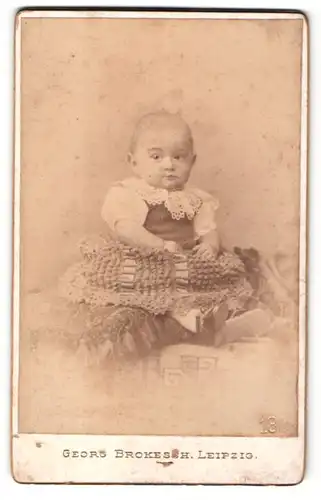 Fotografie Georg Brokesch, Leipzig, Portrait niedliches Baby im hübschen Kleid auf Kissen sitzend