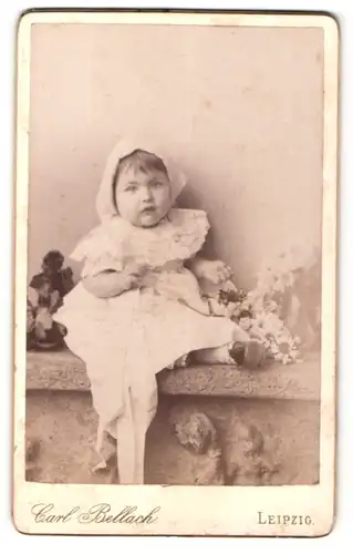 Fotografie Carl Bellach, Leipzig, Portrait sitzendes Kleinkind im hübschen Kleid mit Kopftuch