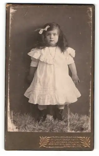 Fotografie Wilhelm Baade Nachf., Stralsund, Portrait kleines Mädchen im weissen Kleid mit Haarschleife