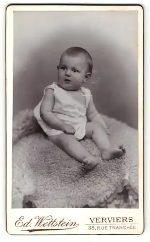 Fotografie Ed. Wettstein, Verviers, Portrait niedliches Kleinkind im Hemdchen auf Decke sitzend