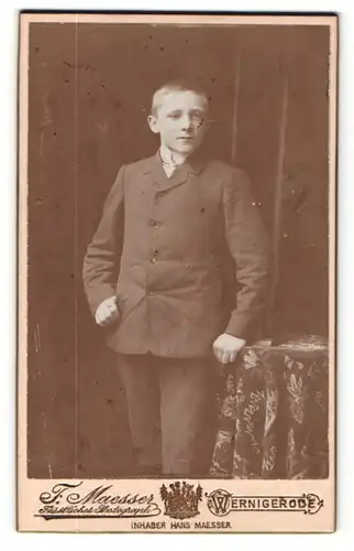 Fotografie F. Maesser, Wernigerode, Portrait halbwüchsiger Knabe im Anzug an Tisch gelehnt