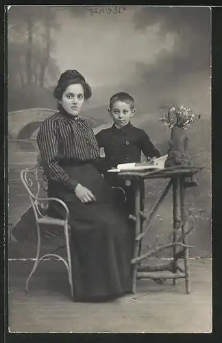 Foto-AK Frau in gestreifter Bluse und kleiner Junge am Tisch vor einer Studiokulisse