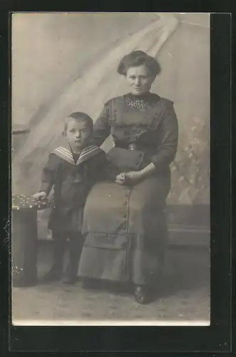 Foto-AK Sitzende Dame mit kleinem Jungen an der Hand vor einer Studiokulisse