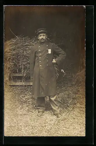 Foto-AK Kriegsgefangener Soldat im Mantel vor einem Strohhaufen