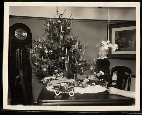 Fotografie Weihnachten, Knabe mit Spielzeug-Flugzeug und Blechauto neben Weihnachtsbaum