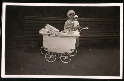 Fotografie Mädchen mit Puppe im Arm und Puppenwagen
