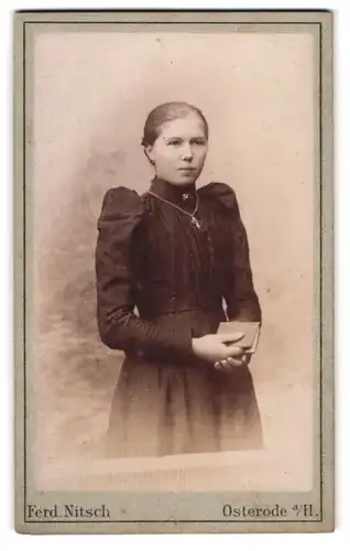 Fotografie Ferd Nitsch, Osterode a. H., Neue Strasse, Junge Frau in schwarzem Kleid mit Zopf und Kreuzkette