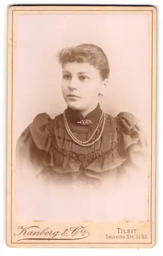Fotografie Kanberg & Cie, Tilsit, Deutsche Str. 31 /32, Junge Frau im schwarzen Kleid mit Perlenkette und Brosche