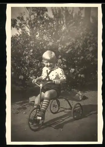 Fotografie blonder Knabe fährt Dreirad