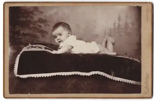 Fotografie C. Stallechner, Trostberg a. Alz., Niedliches Baby in weissem Hemd mit nackten Beinen auf einer Decke