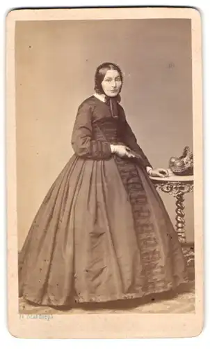 Fotografie F. Brandseph, Stuttgart, Dame im dunklen Reifrock Kleid mit Haube, Onbstkorb auf dem Tisch