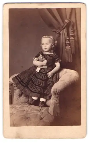 Fotografie Julius Schmidt, Mühlhausen i. Th., niedliches kleines Mädchen mit ihrer Puppe im Arm auf einem Sessel