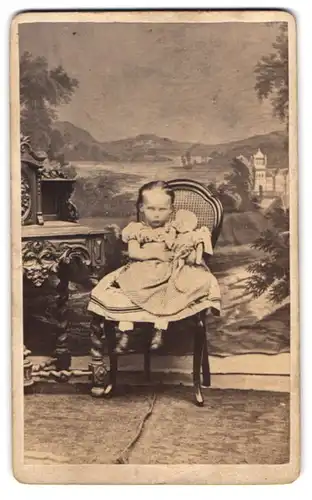 Fotografie unbekannter Fotograf und Ort, niedliches kleines Mädchen mit ihrer Puppe vor einer Studiokulisse