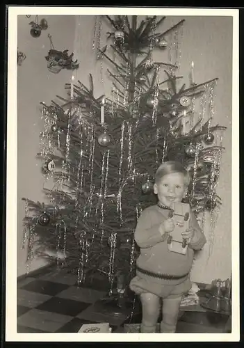 Fotografie Weihnachten, lachender Knabe mit Spielzeug-Holzauto vor dem Weihnachtsbaum stehend