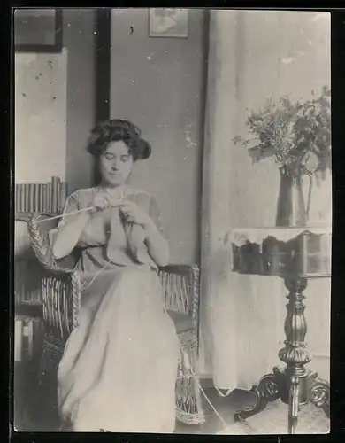 Fotografie junge Hausfrau beim Stricken im Korbsessel sitzend