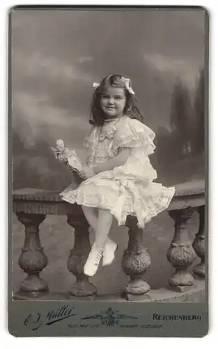 Fotografie E. J. Müller, Reichenberg / Liberec, hübsches kleines Mädchen mit ihrer Puppe auf einer Brüstung sitzend