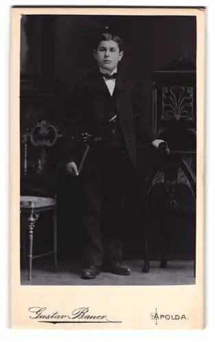 Fotografie Gustav Bauer, Apolda, junger Knabe im dunklen Anzug zu seiner konfirmation, Mappe unterm Arm