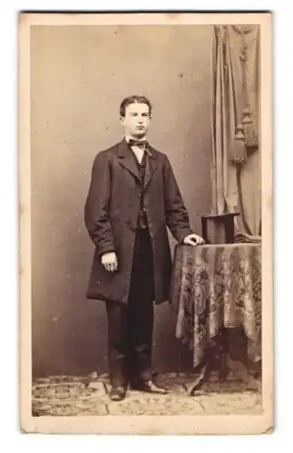 Fotografie W. Filser, Kaufbeuren, junger Mann im Anzug mit Zylinder auf dem Tisch