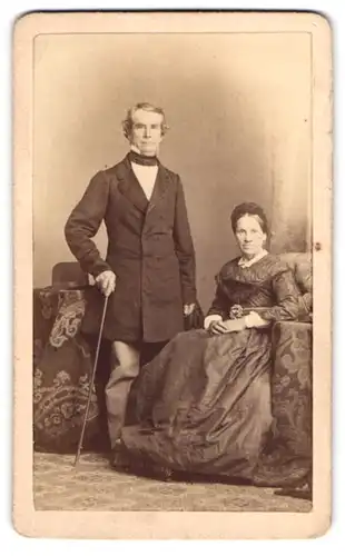 Fotografie C. Höpfner, Halle / Saale, ältere Dame und Mann im Biedermeierkleid und im Anzug mit Flanierstock