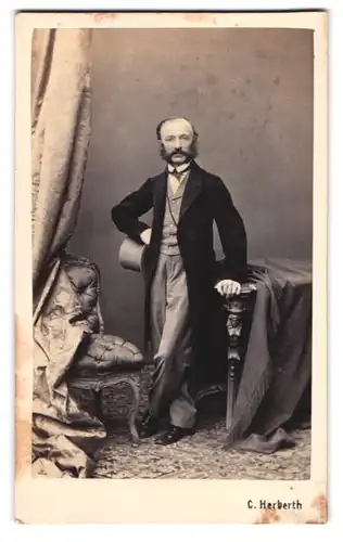 Fotografie C. Herberth, Wien, kleiner Mann im Anzug mit Backenbart und Zylinder in der Hand