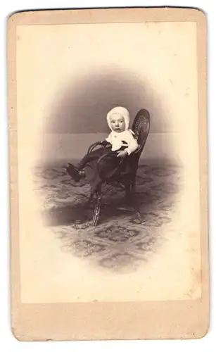 Fotografie Widmayer, Stuttgart, niedliches kleines Kind im Kleid mit Haube sitzt auf einem Stuhl