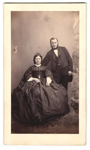 Fotografie unbekannter Fotograf und Ort, Frau im dunklen Reifrockkleid mit Kopfschmuck und Herr im Anzug mit Koteletten