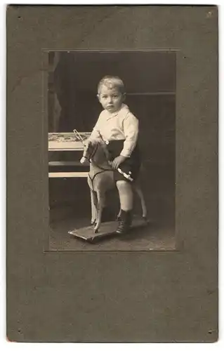 Fotografie unbekannter Fotograf und Ort, junger Knabe sitzt auf seinem Holzpferd