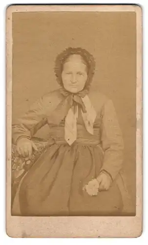 Fotografie unbekannter Fotograf und Ort, Ältere Dame in Kleid mit Kopfbedeckung und Blume