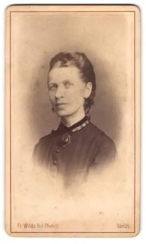 Fotografie Fr. Wilde, Görlitz, Postplatz 3, Junge Dame mit grosser Brosche und Ohrringen im schwarzen Kleid
